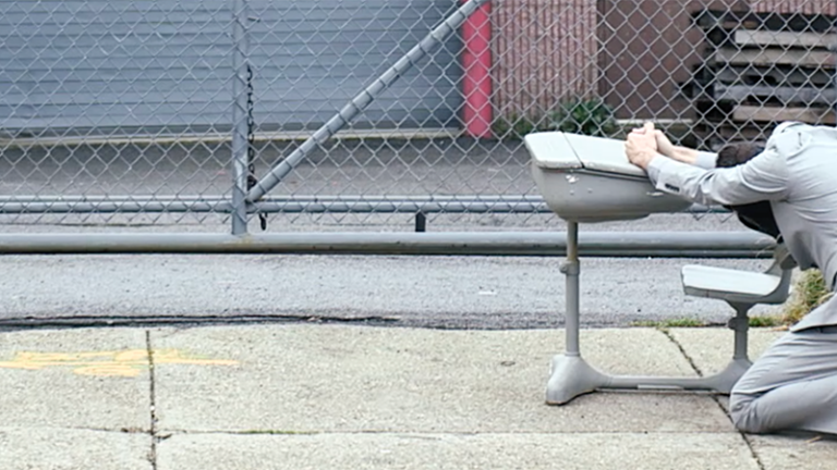 Two people in matching light gray outfits on their knees outside with their hands propped up on a table