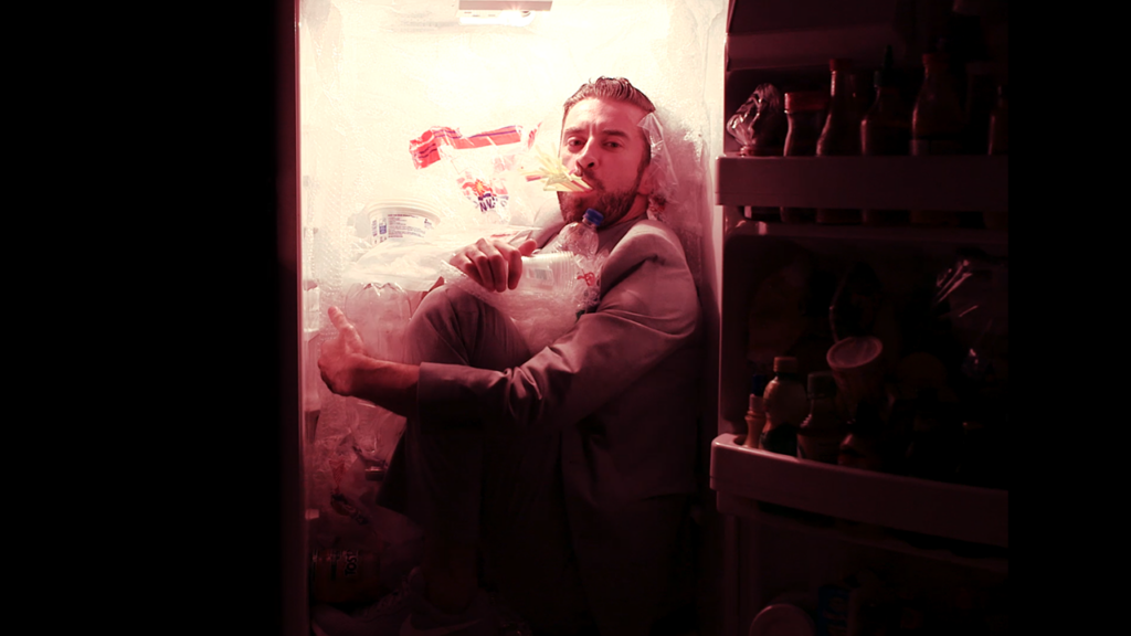 A man sitting in a refrigerator with something in his mouth