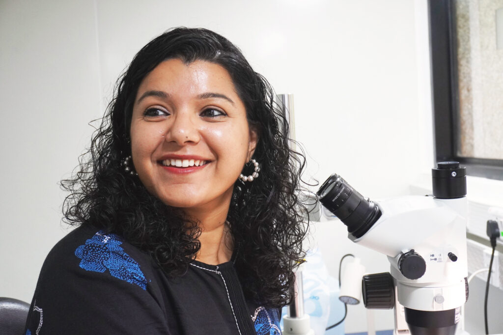 Portrait of Dr. Abhilasha Joshi in her lab, at the microscope.