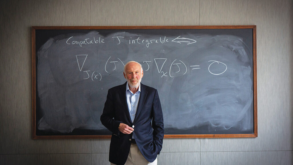 Jim stands in front of a chalkboard. A mathematical equation is written on the board.