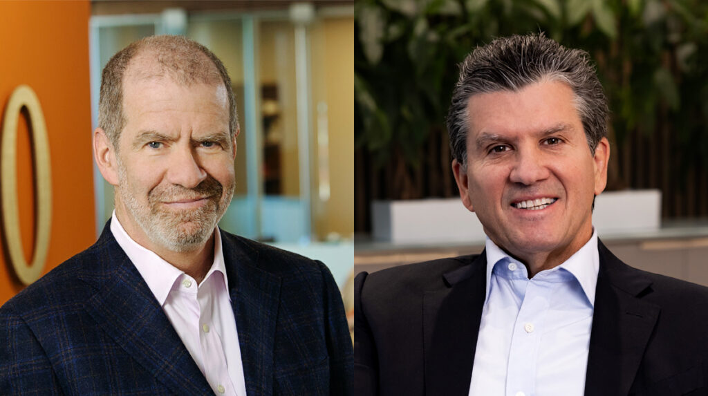 Two middle-aged men in suits are pictured side by side, both smiling. The man on the left has short gray hair and a beard; the man on the right has dark hair and is clean-shaven. Office backgrounds are visible behind them.