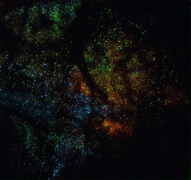 Colorful clusters of green, blue, and orange dots scattered across a dark background, resembling a star field or cosmic nebula in space.