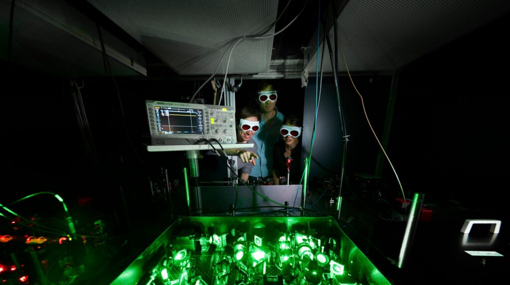 Photo of glowing green tabletop laser equipment with researchers looking on.