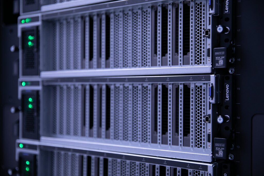 Close-up of several Lenovo server racks with metal grills and green LED lights glowing, indicating powered-on status in a data center environment.