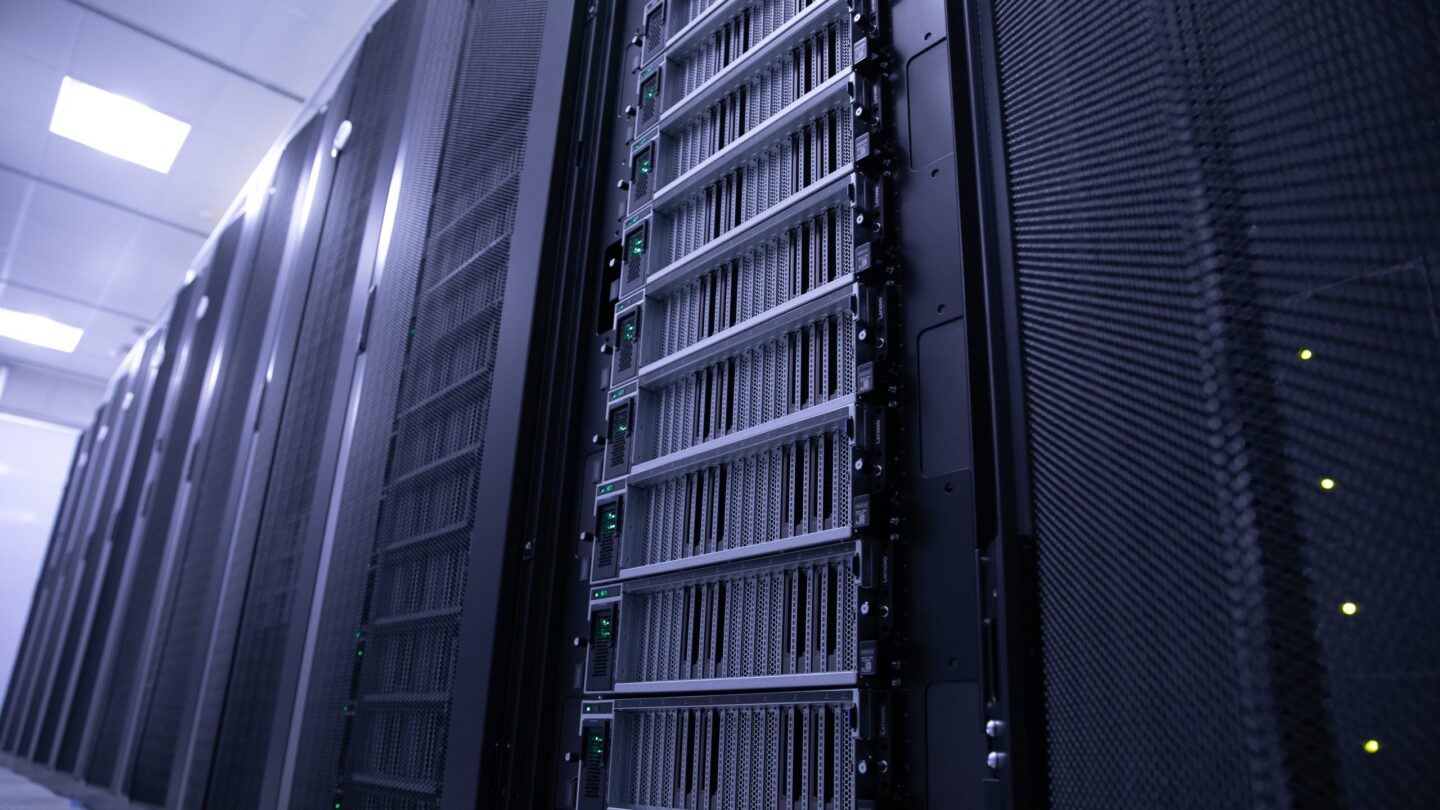 Rows of black server racks with blinking green indicator lights in a brightly lit data center. The image highlights the front view of the servers, emphasizing a clean, high-tech environment.
