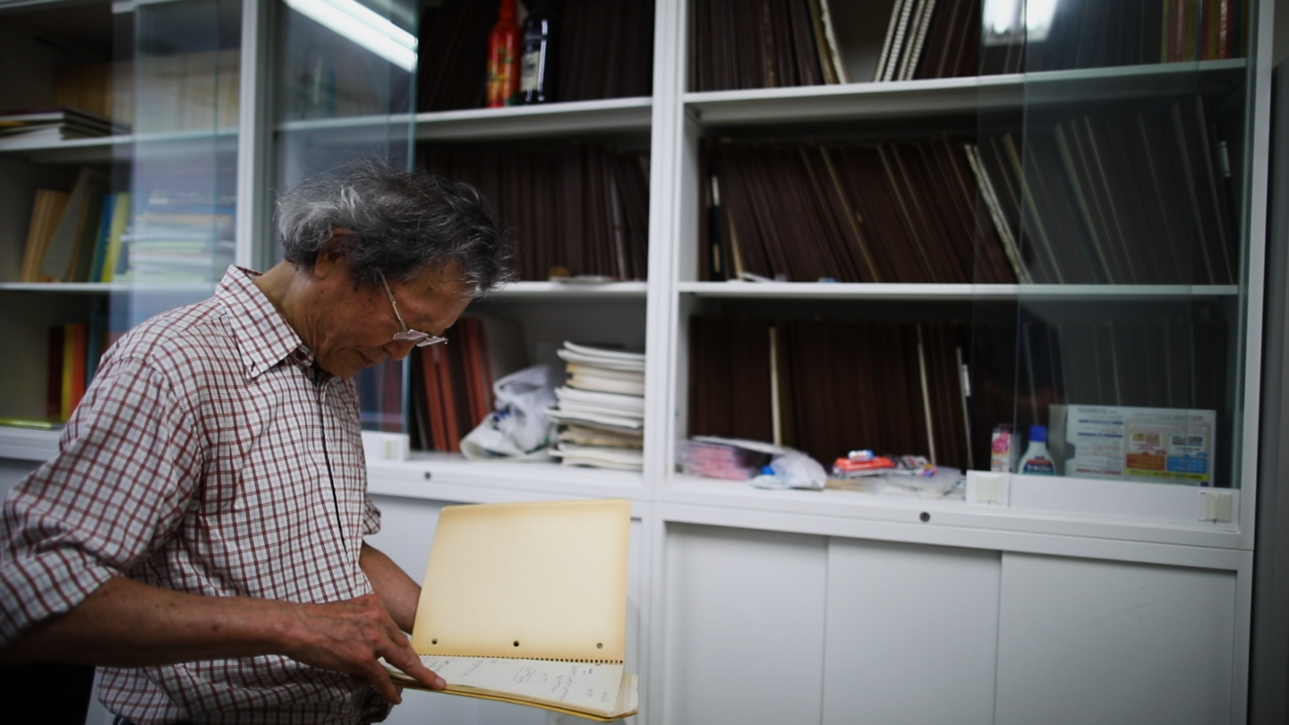 Masaki Kashiwara looking at a folder in front of shelves full of folders