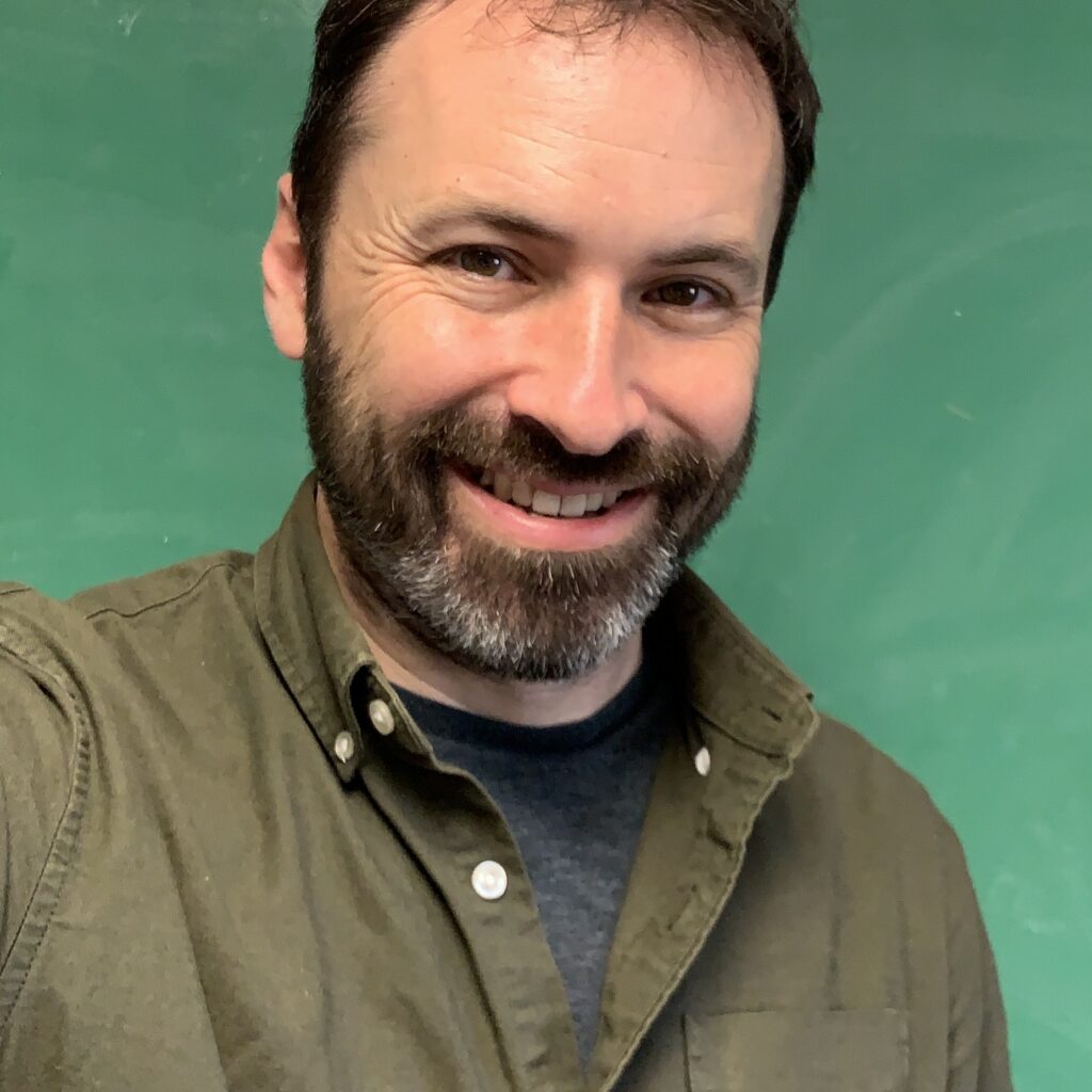 Scott McKinley in front of a green chalkboard