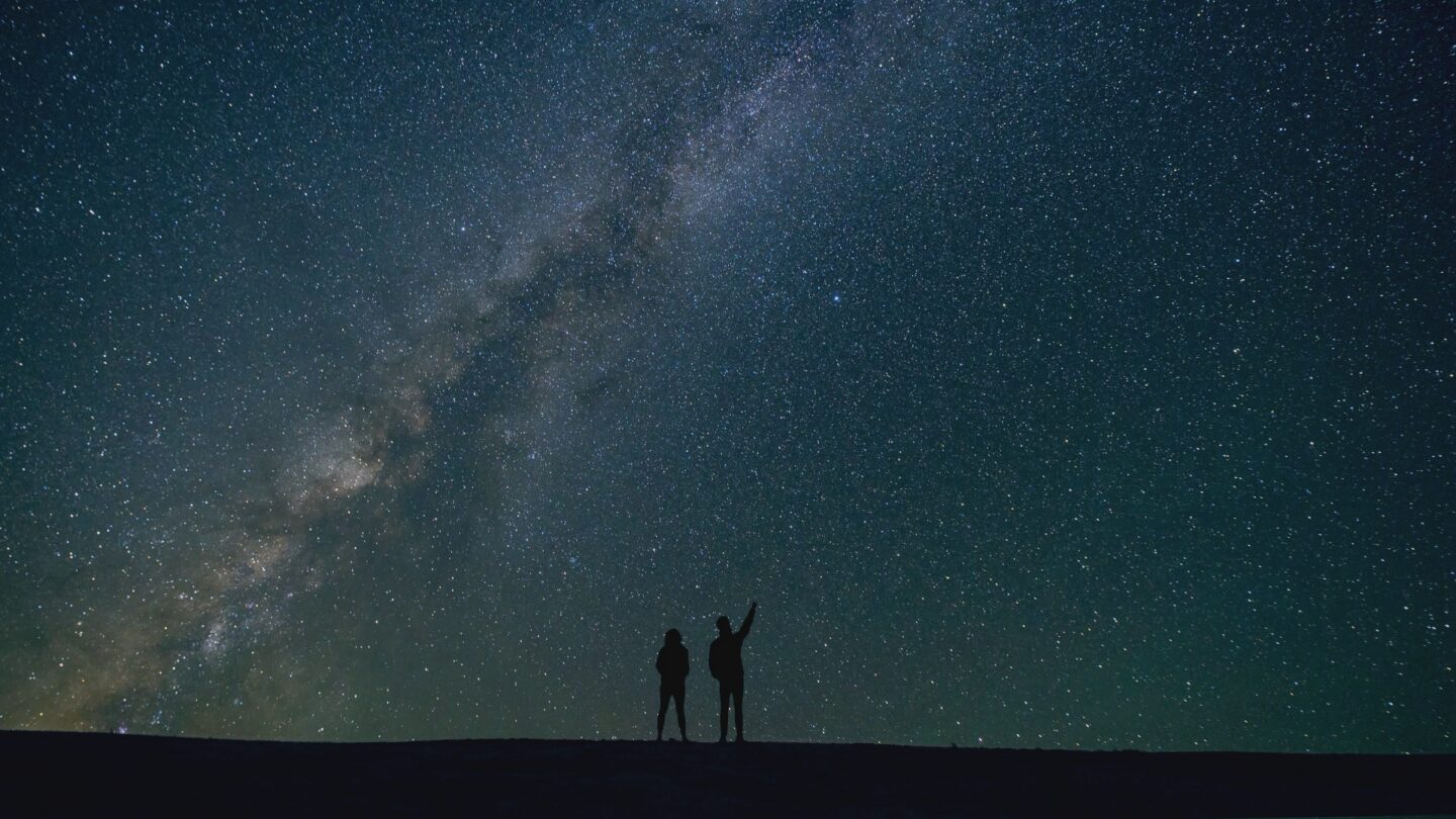 Two people pointing to the night sky
