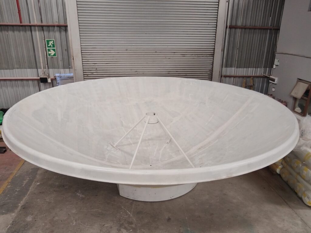 A large white satellite dish stands indoors on a concrete floor, surrounded by metal walls and a closed roller door in an industrial setting.
