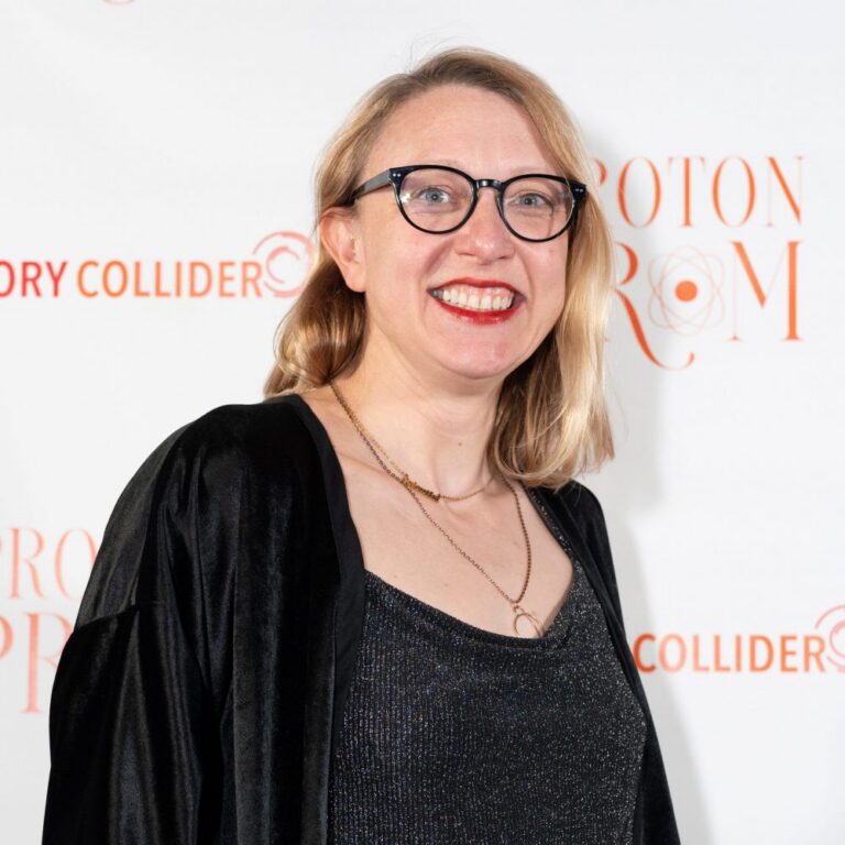 A smiling person with shoulder-length blonde hair, glasses, and a black outfit stands in front of a white background with orange text and logos.