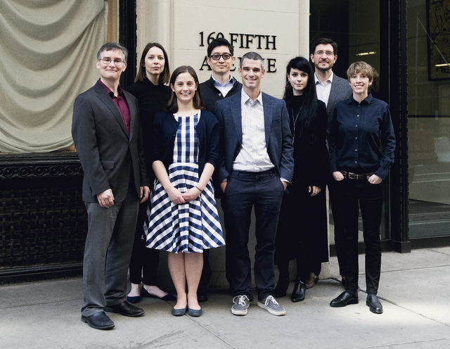 Eight people stand together outside a building at 169 Fifth Avenue, posing for a group photo. Most are dressed in business attire, with one person in a striped dress.