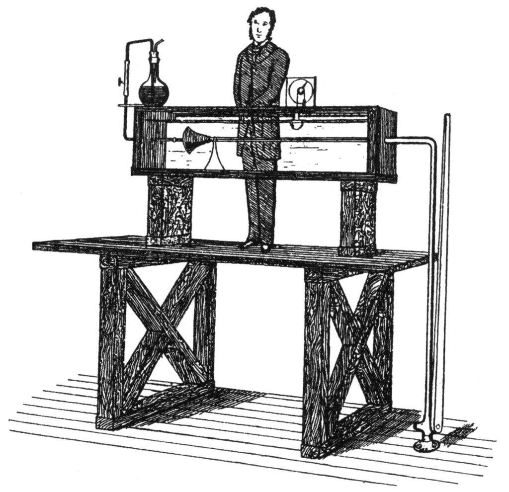 A black and white illustration of a person standing behind a large scientific apparatus on a table, with glassware, tubes, and a manometer attached.