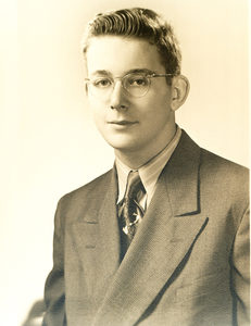A young man wearing glasses, a suit, and a tie poses for a formal portrait in sepia tones. He has short, neatly styled hair and a neutral expression.