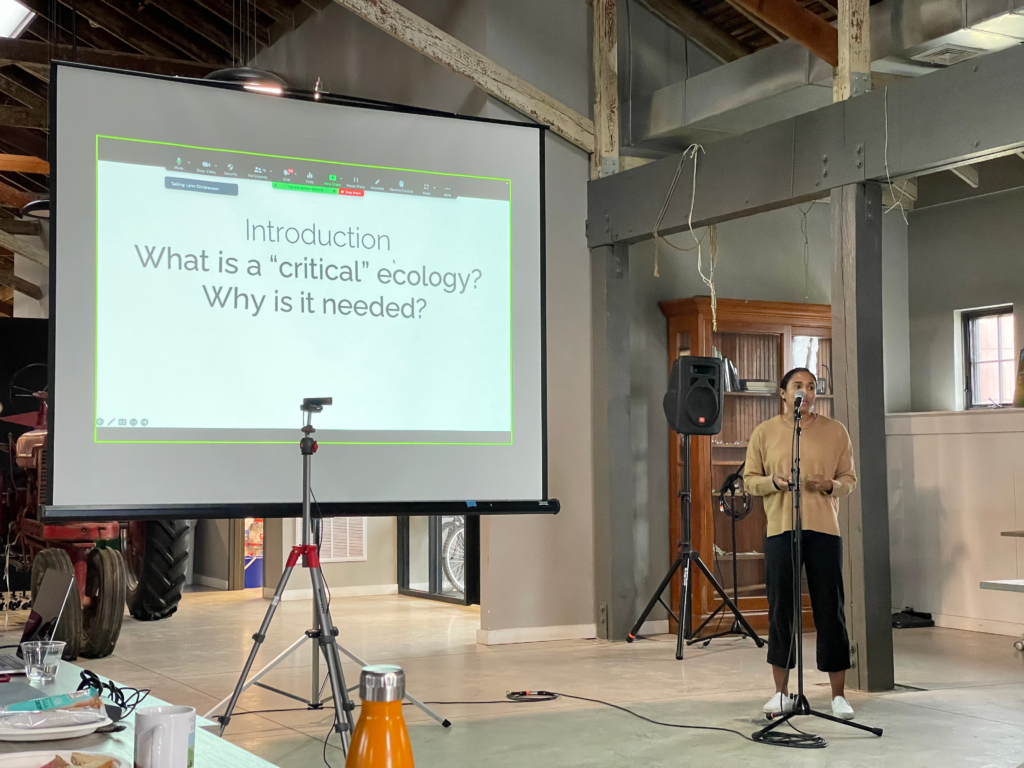 Suzanne Pierre standing at a mic making a presentation with a projector screen
