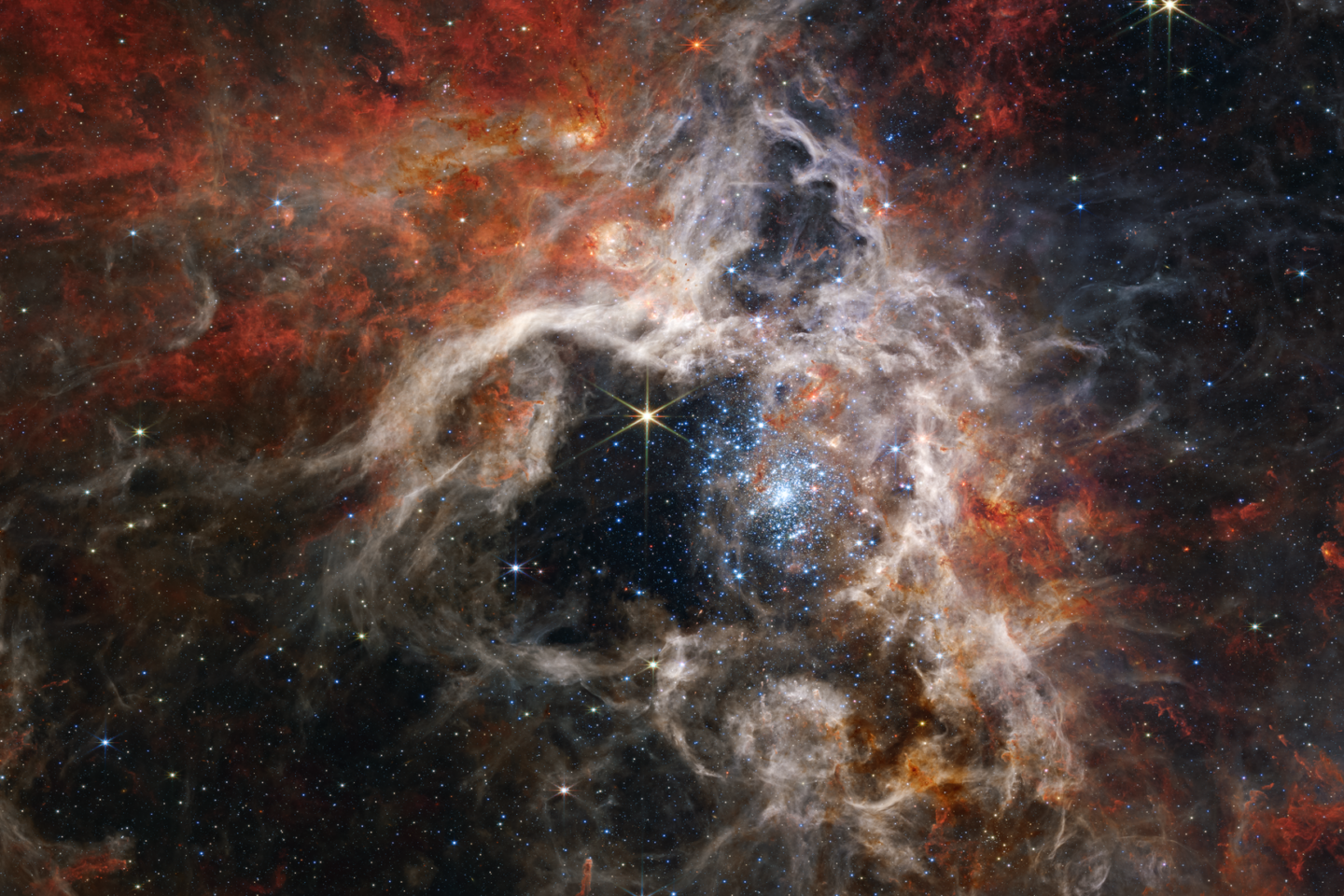 A vibrant star cluster shrouded by red, orange, and gray clouds of cosmic gas and dust in deep space, with numerous stars scattered across the scene.