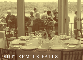 A round table set for a meal overlooks a group of people standing and talking near a window, with trees and water visible outside. Text reads BUTTERMILK FALLS..