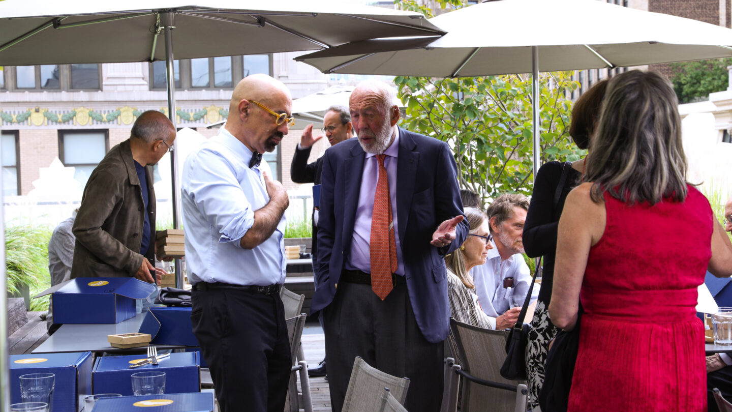 A photograph of a group of people in an outdoor space with seats and umbrellas.