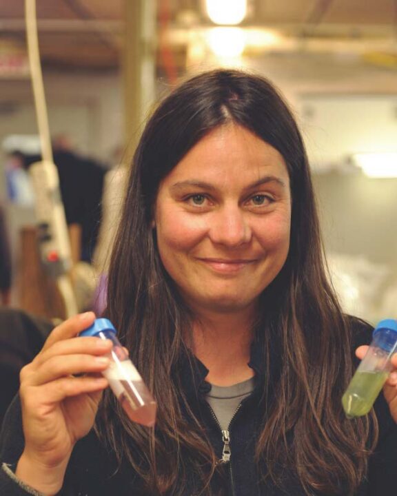 Angelicque White holding a vial of green liquid in her left hand and a vial of pink liquid in her right hand