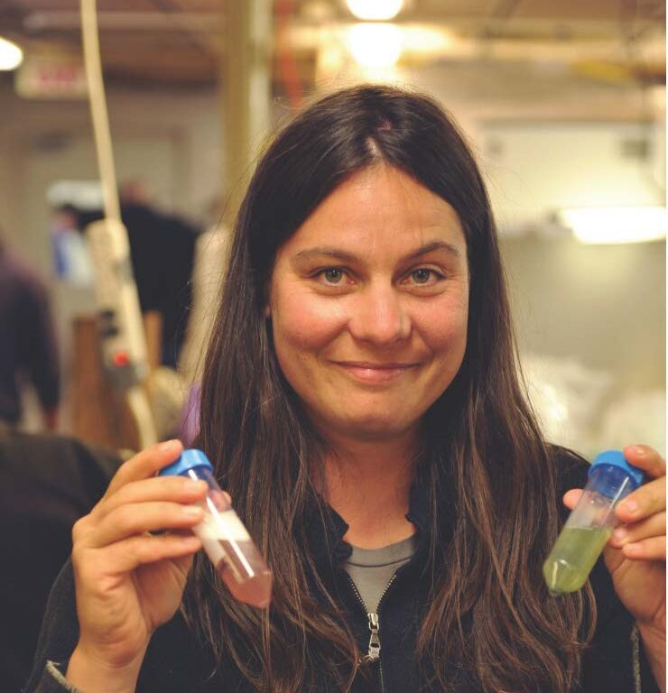Angelicque White holding a vial of green liquid in her left hand and a vial of pink liquid in her right hand