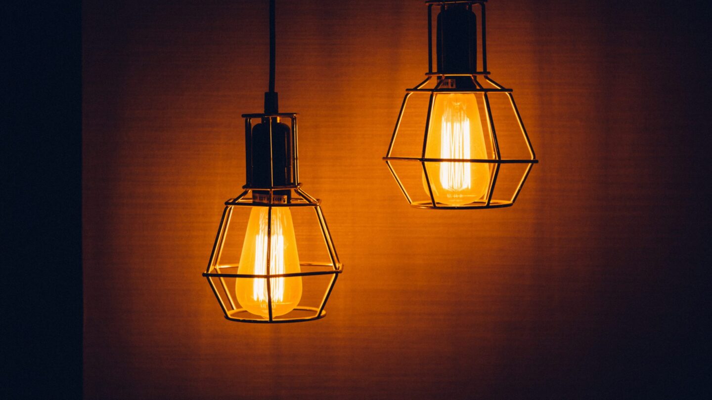 Two similar-looking lightbulbs shine while hanging from the ceiling.