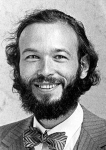 Black and white photo of a smiling man with a full beard and wavy hair, wearing a pinstriped suit, white shirt, and a bow tie.