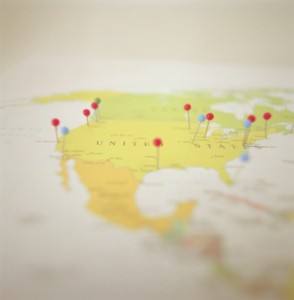 A map of the United States with red and blue pushpins marking various locations across the country. The image is softly focused, with the pins and map features slightly blurred.