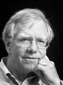 Black and white portrait of an older man with light hair and glasses, resting his chin on his hand, looking thoughtfully at the camera.