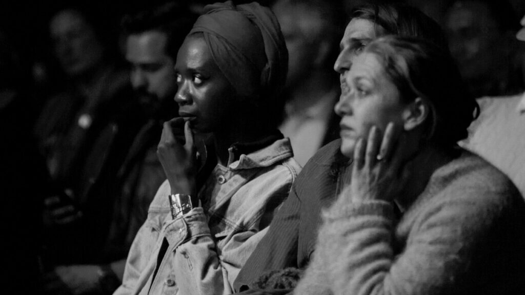 Grayscale image of people sitting in a crowd while staring intently ahead