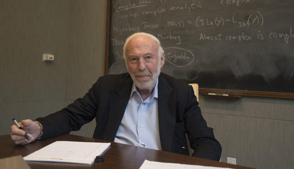 Jim Simons sitting in front of chalkboard.