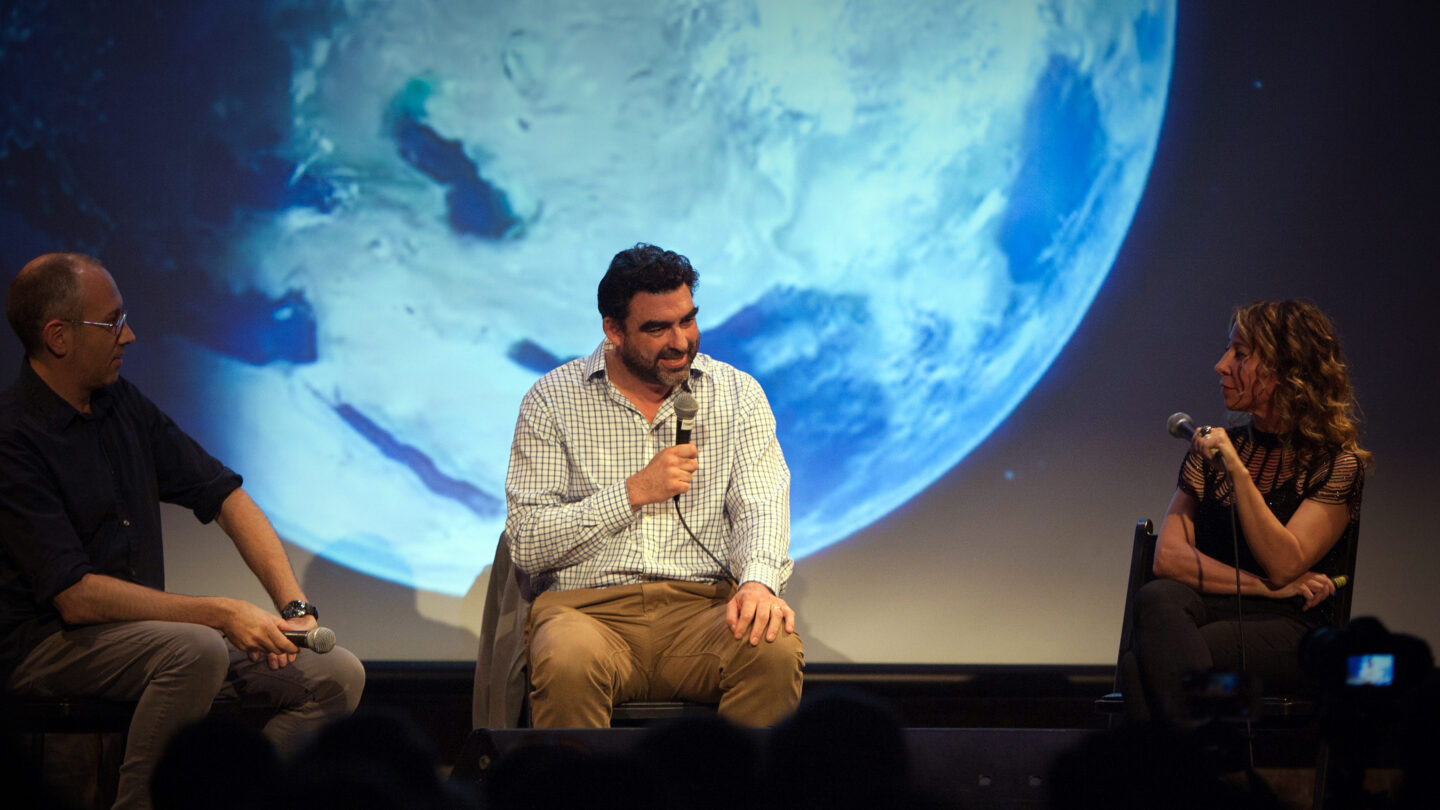 Three people sitting on a stage and talking into microphones