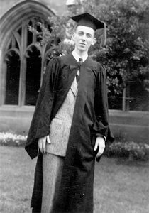 Young person in graduation cap and gown stands outside near a stone building with arched windows and greenery. The black-and-white photo has an old-fashioned, vintage appearance.