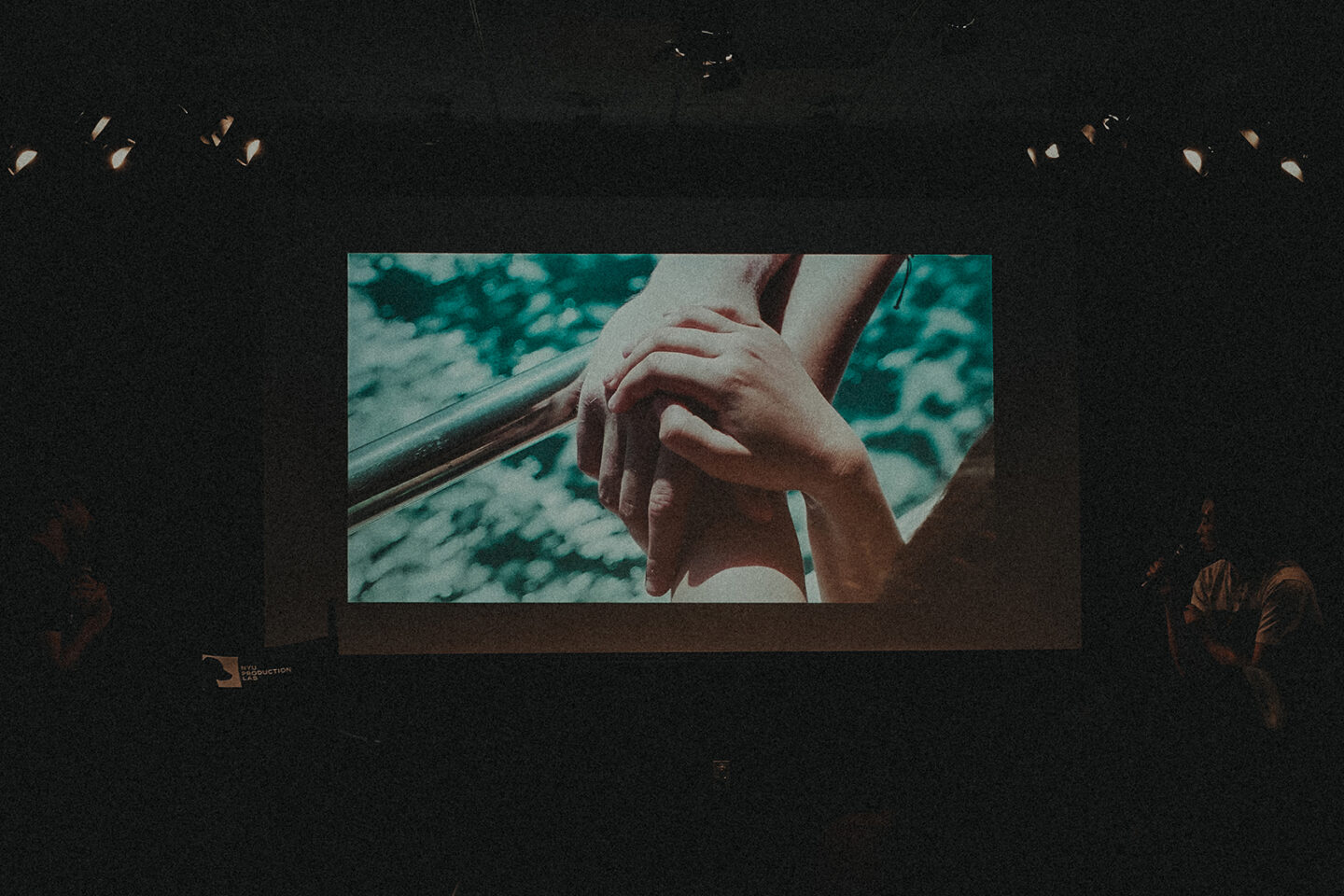 A photo taken at the screening of 'Symbiosis,' showing a dark auditorium with a film still of two clasped hands on the screen.