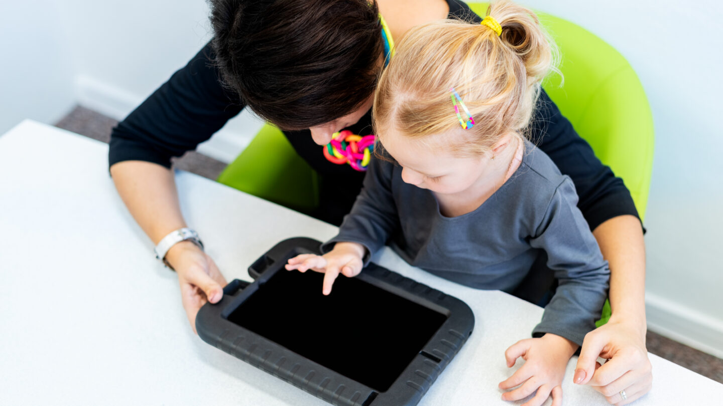 Woamn helping a child learn with tablet.
