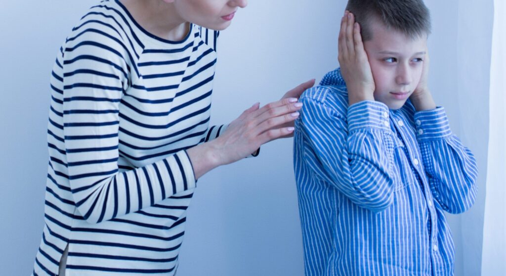 Photo of Boy with autism spectrum disorder covers his ears during a therapeutic session.