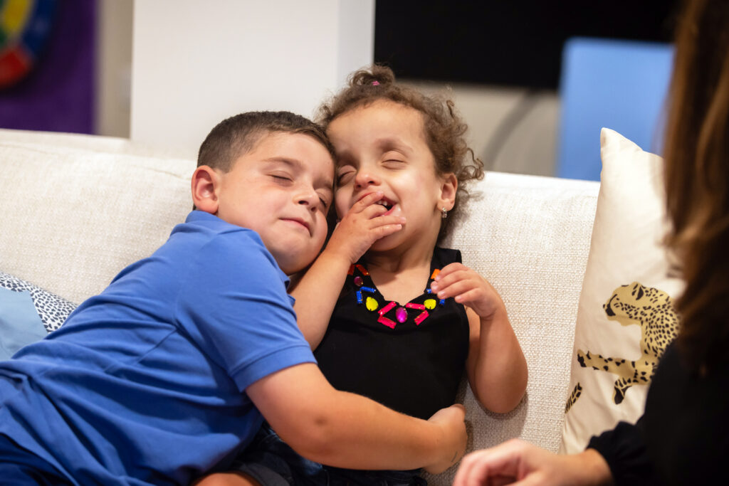 Two children cuddle on a sofa.