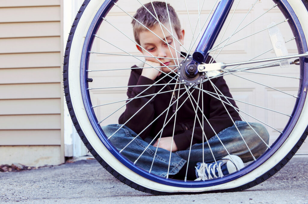 A photo of a boy looking at the one flat tire of the bicycle.