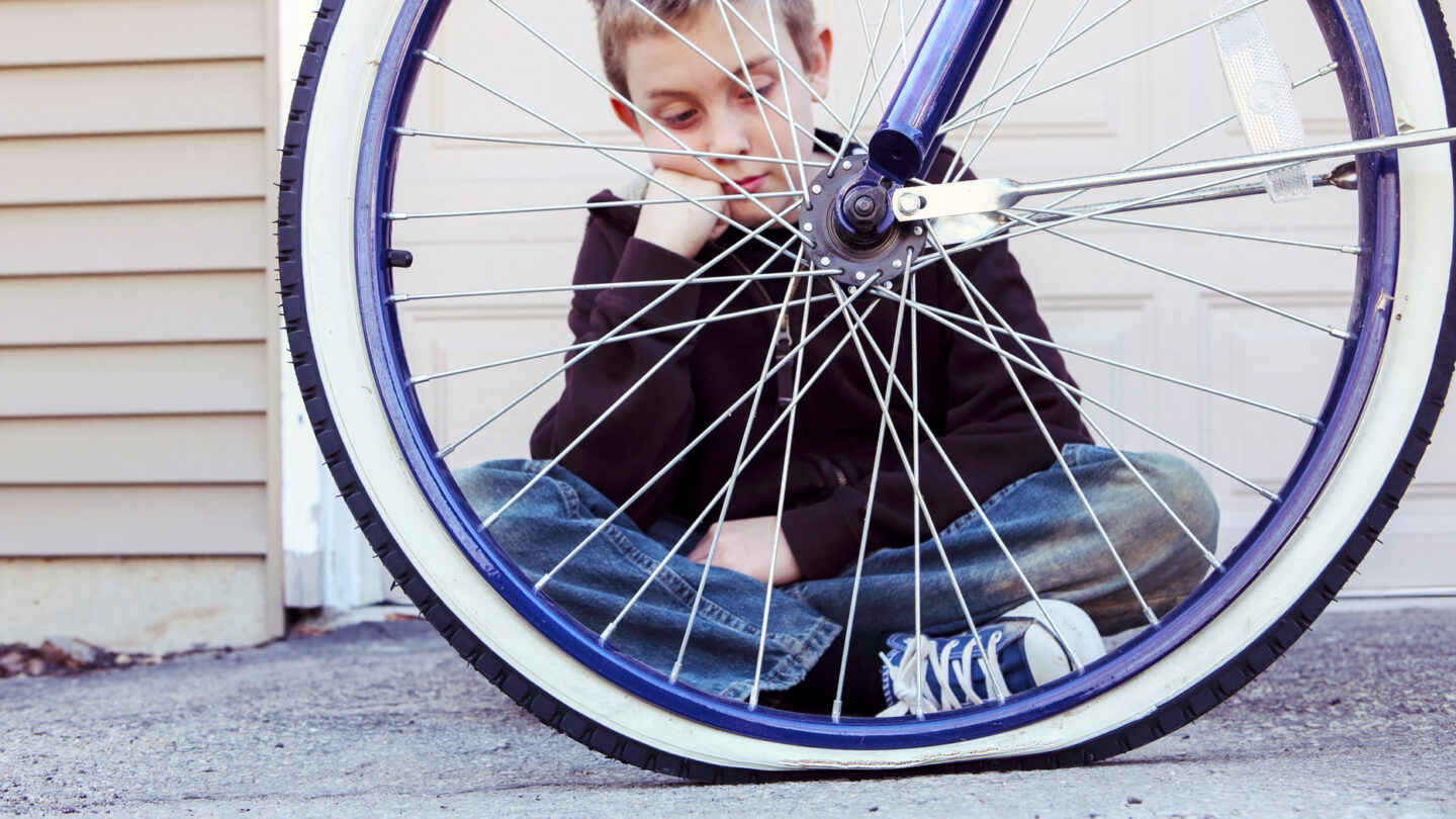 A photo of a boy looking at the one flat tire of the bicycle.