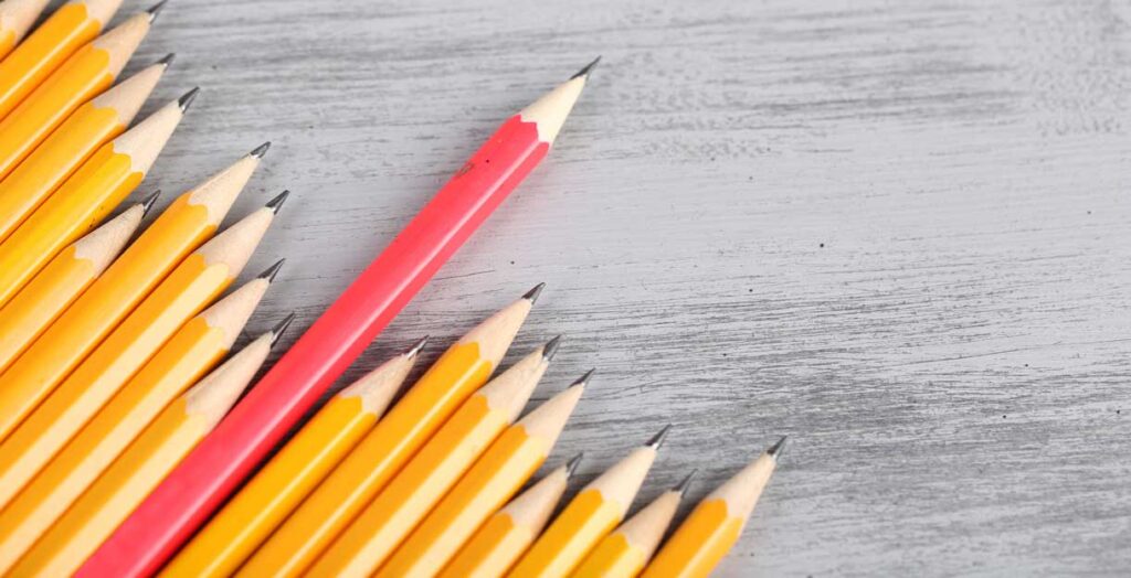 A group of sharpened yellow pencils lies on a gray wooden surface, with one red pencil among them standing out.
