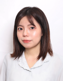 A woman with straight, shoulder-length dark hair and light skin wears a white collared blouse, looking at the camera with a neutral expression against a plain white background.
