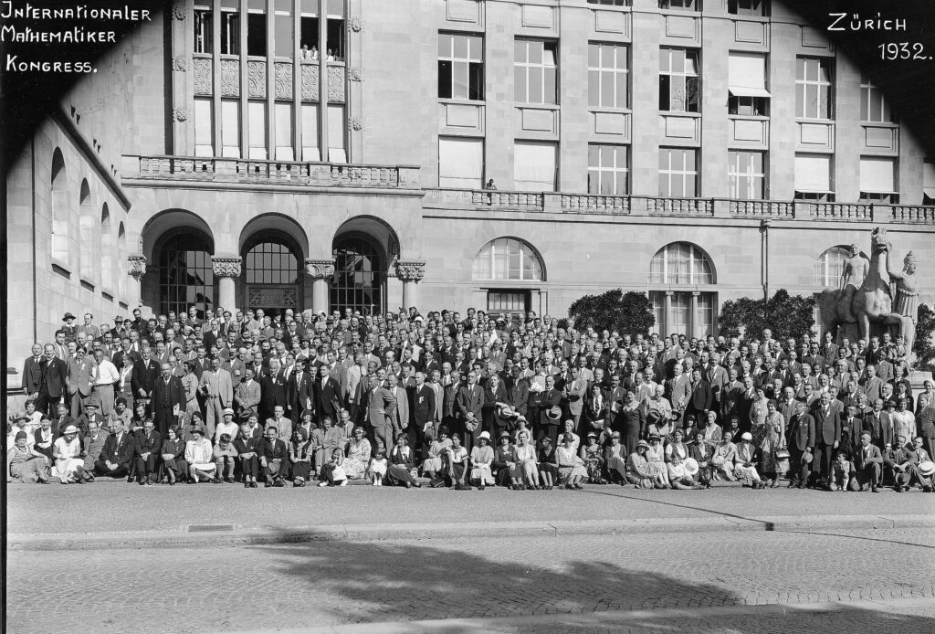 A large group of people pose for a photo in front of a grand building with arched windows and a statue, labeled Internationaler Mathematiker Kongress, Zürich 1932..
