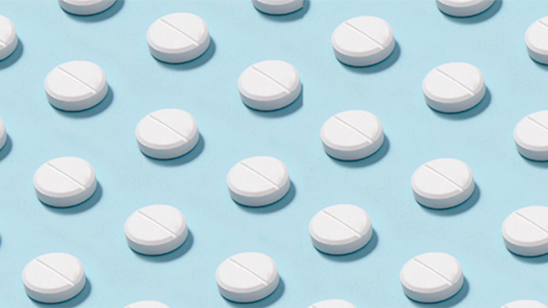Rows of white round tablets, each with a scored line, arranged in a neat diagonal pattern on a light blue background.