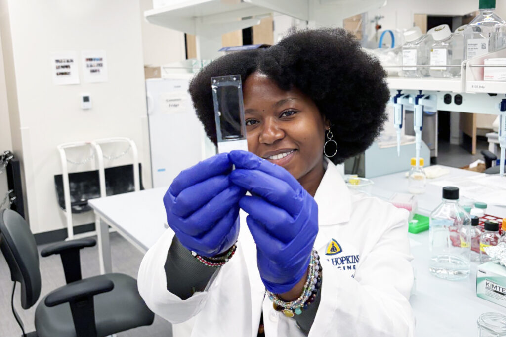 A photo of Florence Njoroge in the lab, holding a slide containing 10-µm zebra finch brain sections.