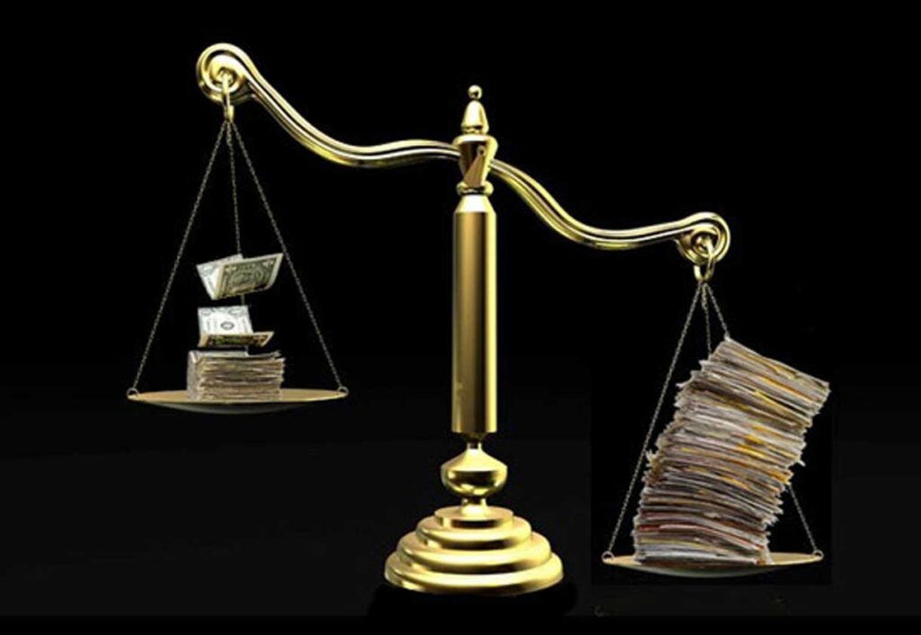 A gold balance scale with stacks of money outweighing a larger stack of papers, set against a black background.