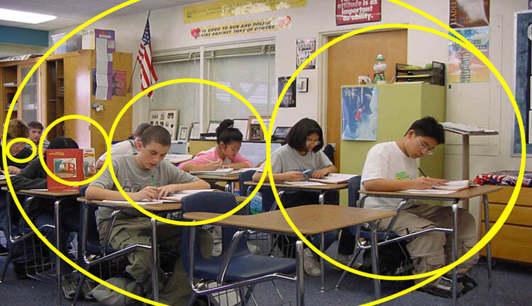 Students sit at desks in a classroom, writing on papers. A yellow Fibonacci spiral overlays the image, curving around the students and desks. Shelves, posters, and an American flag are visible in the background.