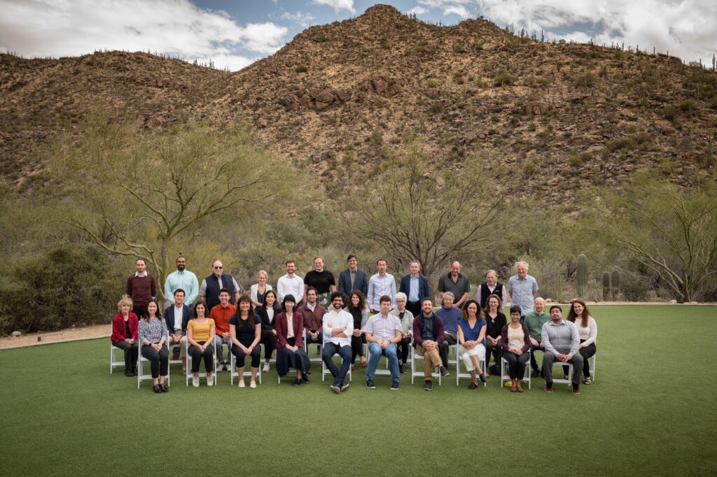 A photograph of the Simons Foundation Society of Fellows sitting in chairs in an outdoor scene.