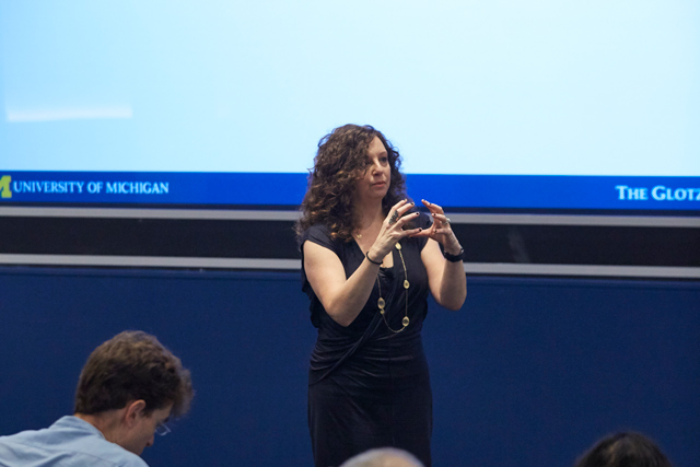 Woman gesticulating with two hands as she stands in front of a lecture hall