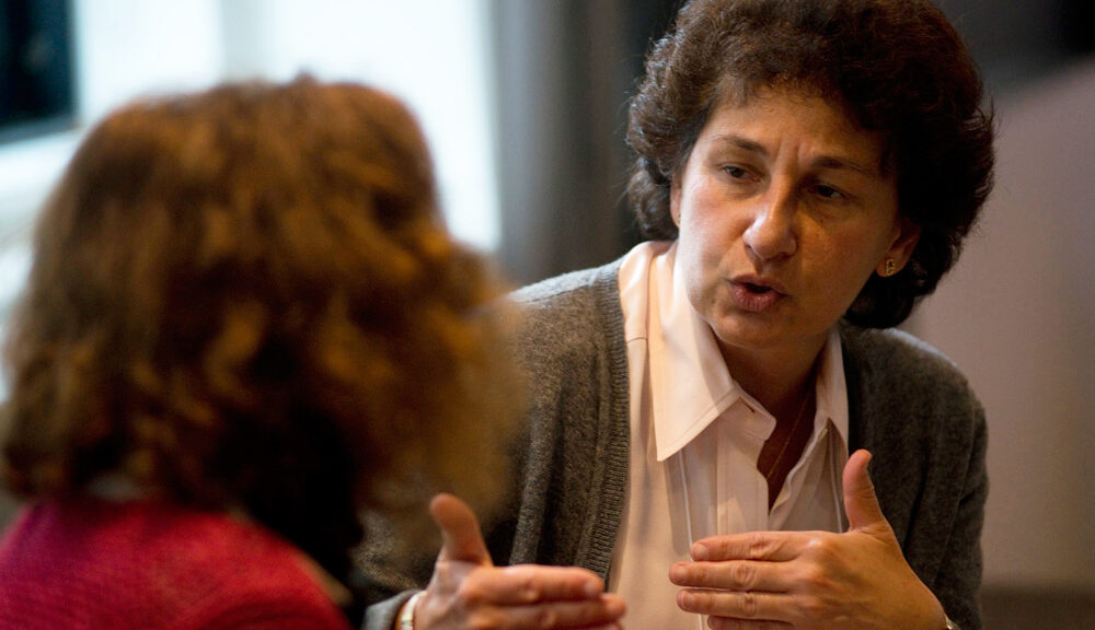 Two people sitting and talking with each other as one person gesticulates with both hands