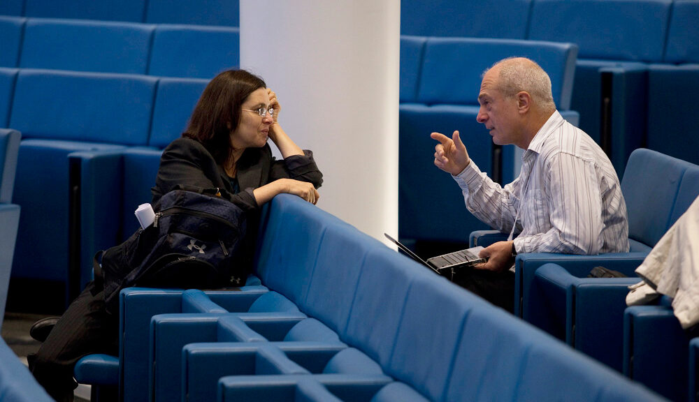 Two people sitting in different rows of an almost empty lecture hall, while talking