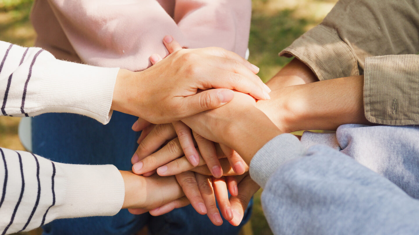 A close-up of diverse multiracial men and women group with stacking hands on top of each other, suggestive of a support group.