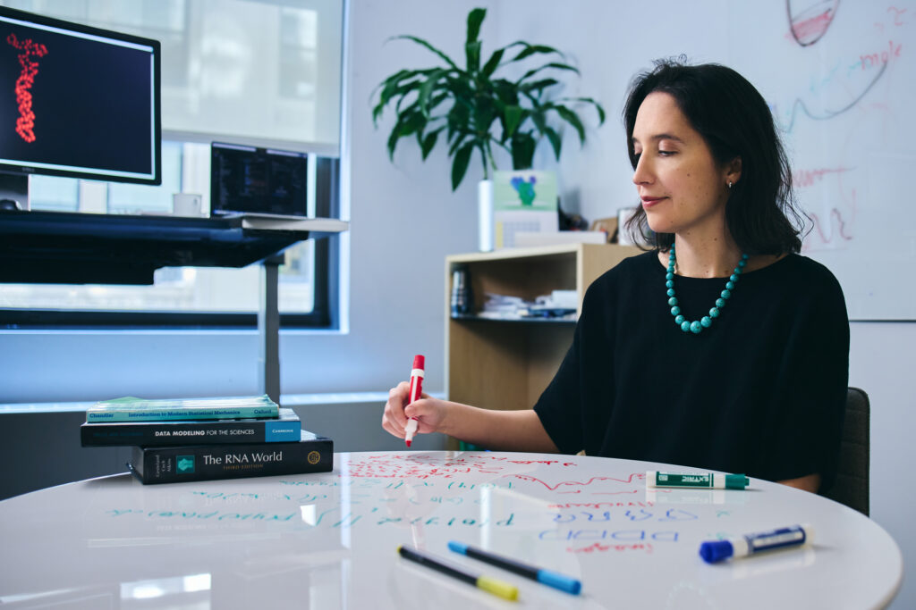 A photo of Pilar Cossio in her office, writing on her whiteboard table with a dry-erase marker.